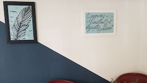 Una habitación con dos sillas rojas, una pequeña mesa redonda con una planta, una obra de arte enmarcada y un cartel motivacional en la pared.