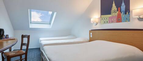 A hotel room with a single bed, a desk with a chair, a small window, and a cityscape painting on the wall.