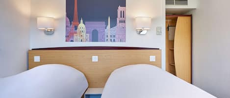 Ein Hotelzimmer mit zwei Einzelbetten, einem an der Wand befestigten Kunstwerk mit Pariser Sehenswürdigkeiten und zwei Wandleseleuchten.