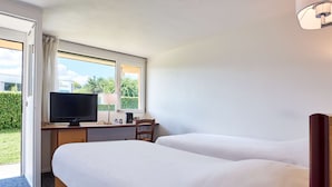 Habitación de hotel con dos camas, un escritorio con televisor y una ventana con vista a zonas verdes.