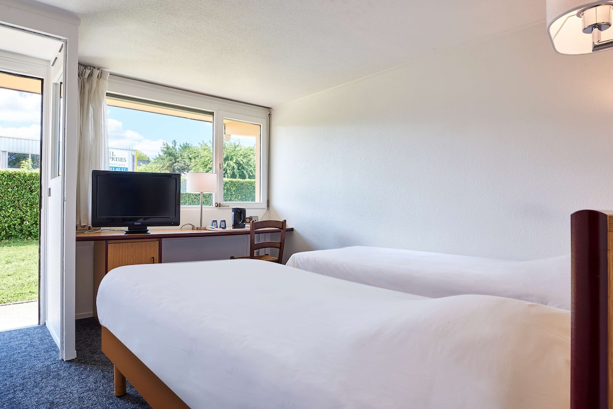 Une chambre d’hôtel avec deux lits, un bureau avec une télévision et une fenêtre donnant sur un paysage verdoyant.