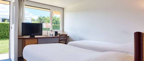 Quarto de hotel com duas camas, uma escrivaninha com televisão e uma janela com vista para o verde.