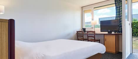A hotel room with a single bed, a desk with a chair, a television, and a window with curtains.