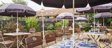 An outdoor dining area with tables and chairs, umbrellas, and a view of a building in the background.