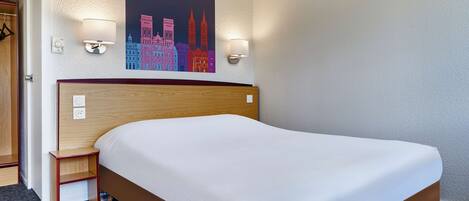 Una habitación de hotel con una cama grande, una mesita de noche pequeña, un cuadro colgado en la pared y dos apliques.