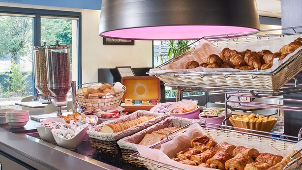 Un bufé con diversos alimentos, entre ellos pan, pasteles y una estación de café.