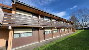 Un hotel de dos pisos con techo plano, varios balcones y un césped.