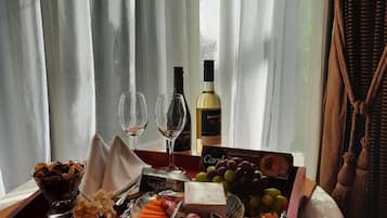 Un vassoio con snack, bicchieri da vino e una bottiglia, su un tavolo vicino a una finestra con tende leggere.