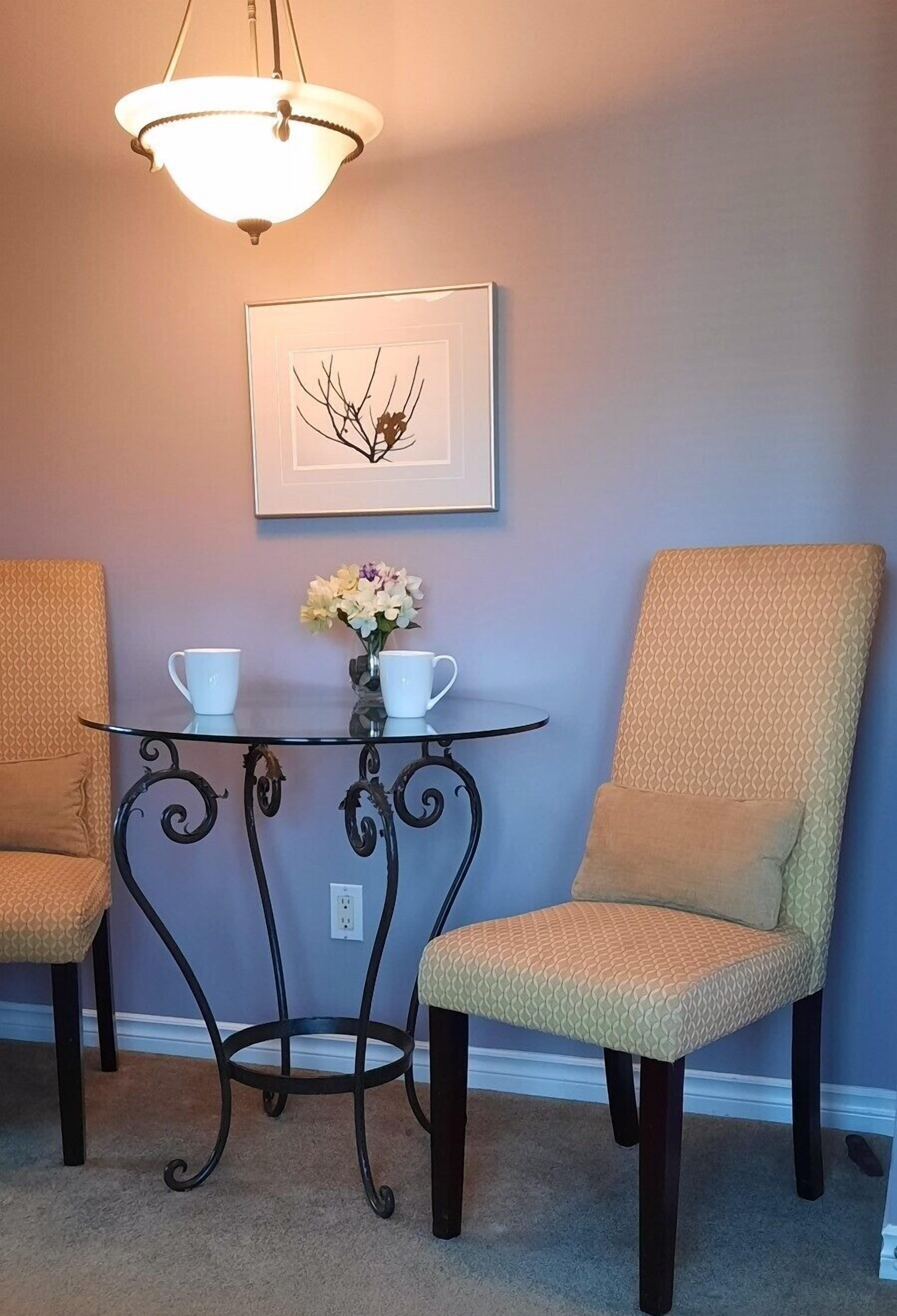 Un coin repas comprenant deux chaises, une petite table, un vase avec des fleurs et un tableau encadré accroché au mur.