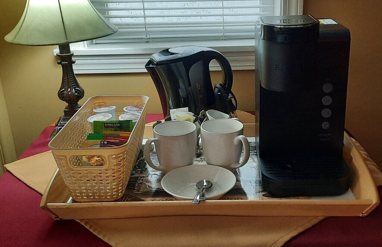 A breakfast tray with a coffee maker, two mugs, a plate, and a basket of cereal.