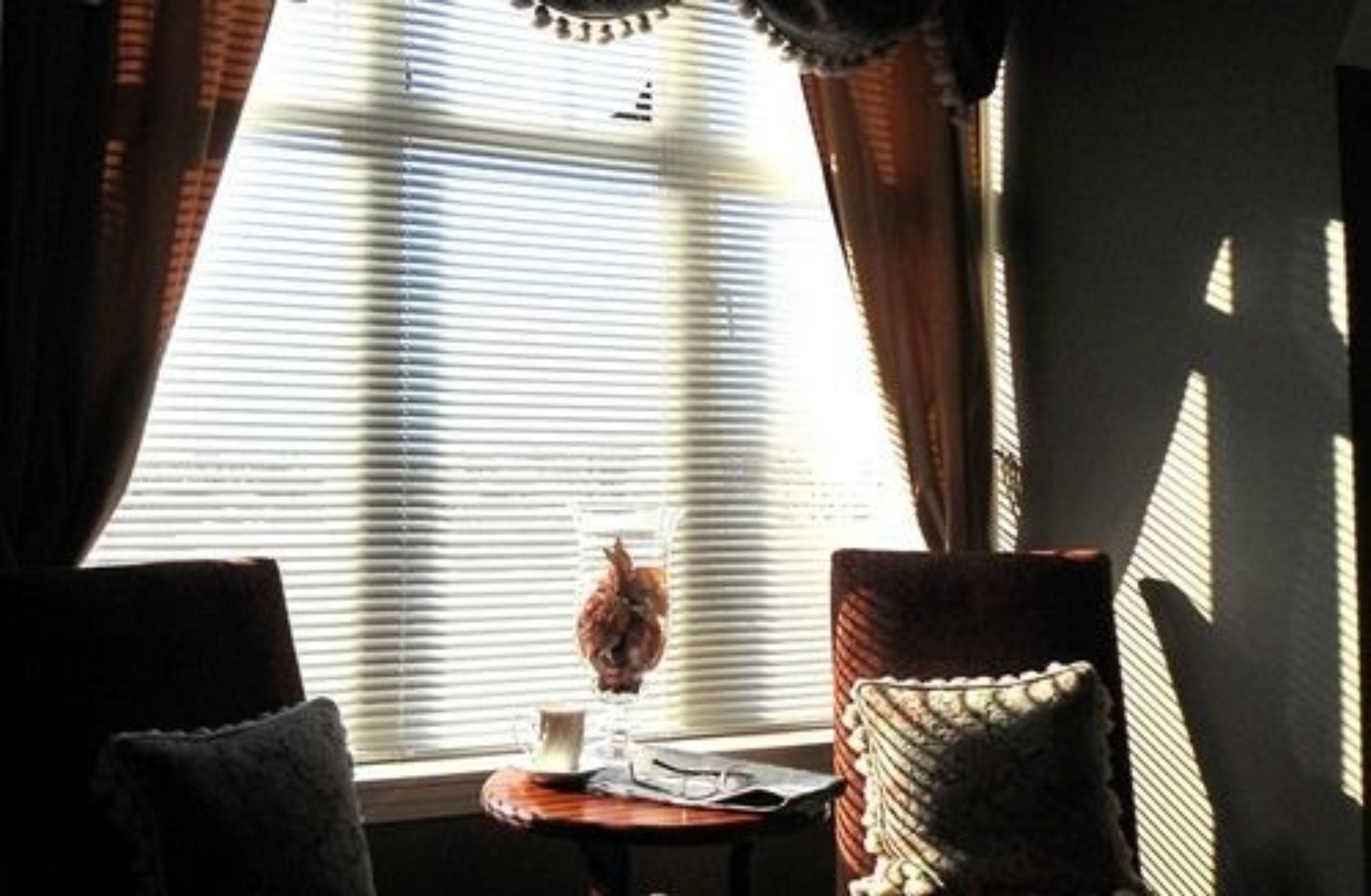 A room with a window, a small table with a vase and a cup, and two chairs.
