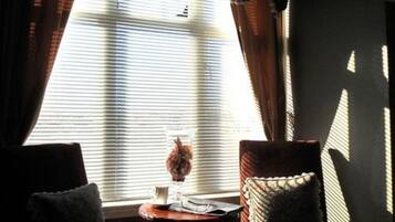 A room with a window, a small table with a vase and a cup, and two chairs.
