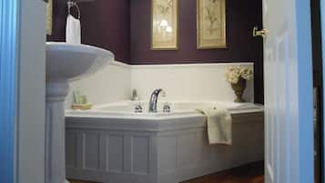 A bathroom with a freestanding bathtub, a pedestal sink, and two framed floral paintings on the wall.