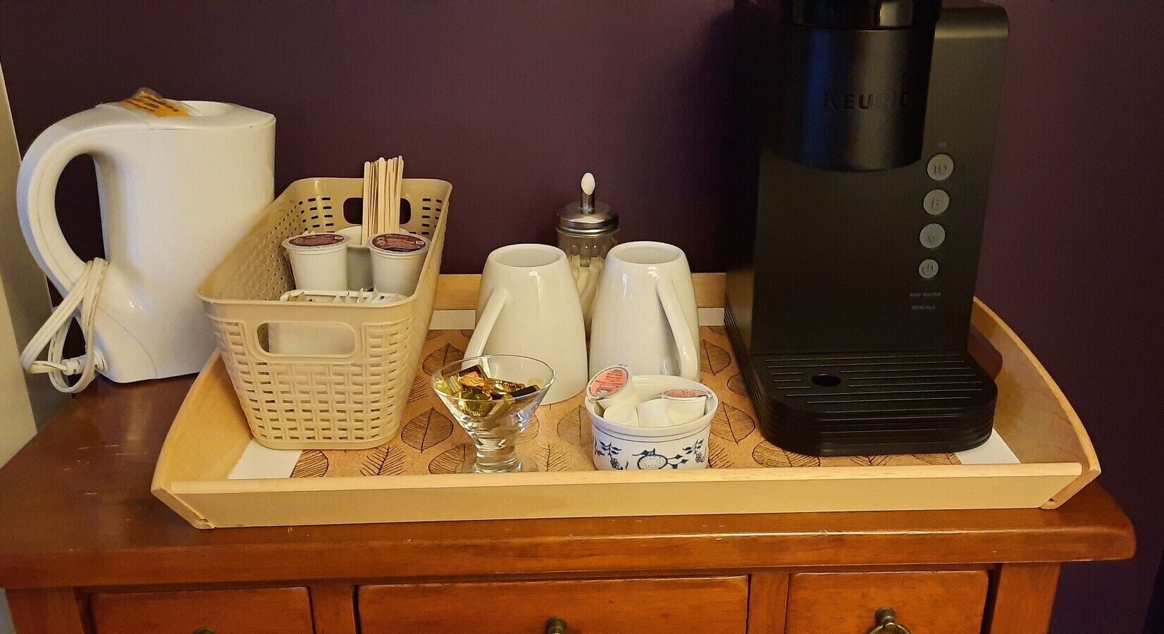 Eine Kaffeemaschine, ein Wasserkocher, ein Tablett mit Tassen und eine Servierplatte auf einer Holzoberfläche.