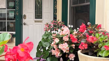 Una puerta principal con una placa con número, una maceta colgante y diversas plantas en macetas.
