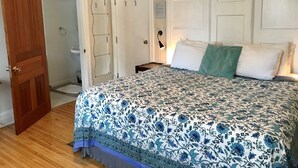 A bedroom with a floral-patterned bedspread, a wooden door, and a white wall with a mirror. - Ellis House B&B, Niagara Falls (Niagara Falls)