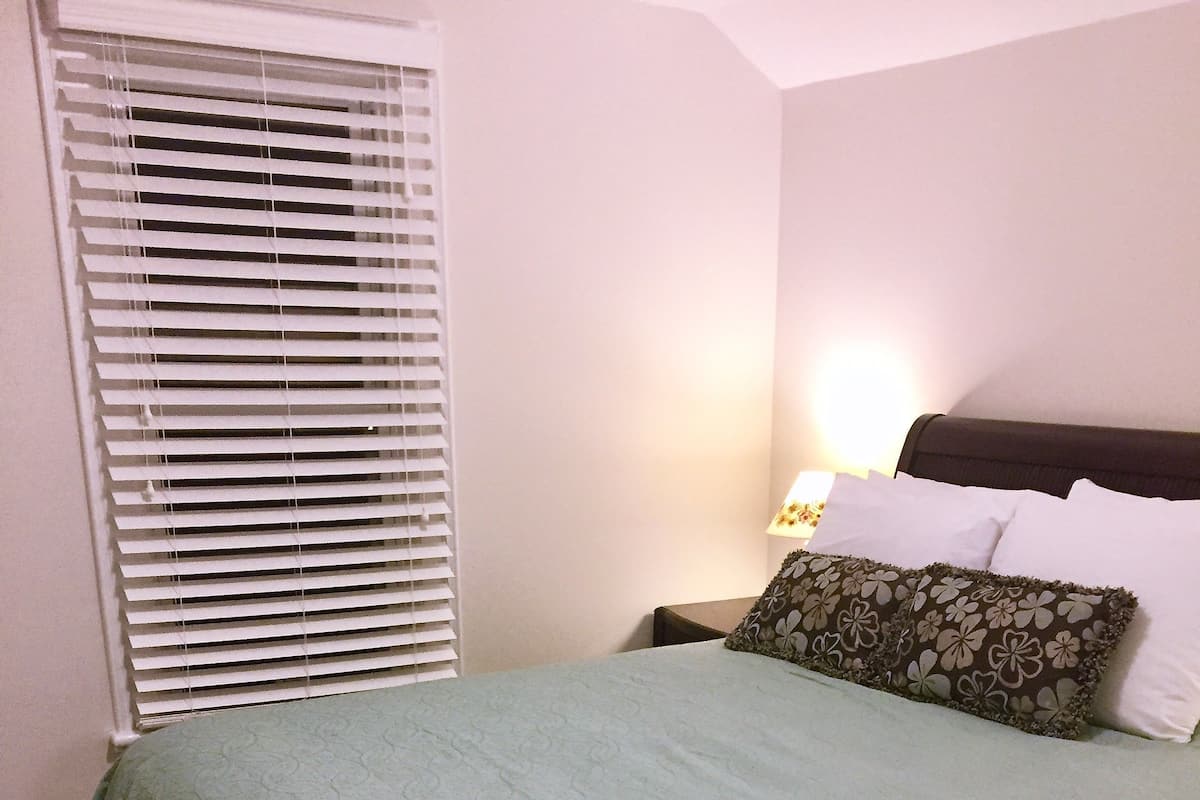 A neatly made bed with a green bedspread, white pillows, and a single decorative pillow with a floral pattern.