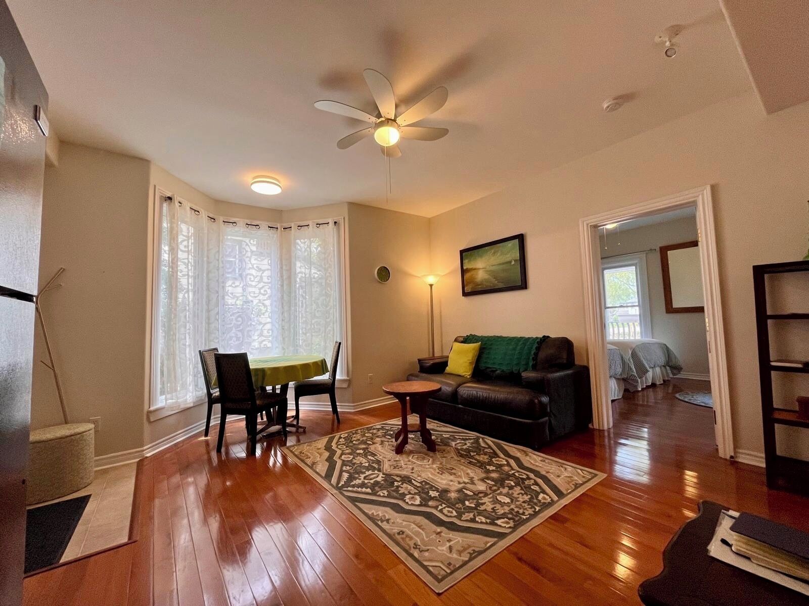 A living room with a dining table, a sofa, a patterned rug, a ceiling fan, and a painting on the wall.