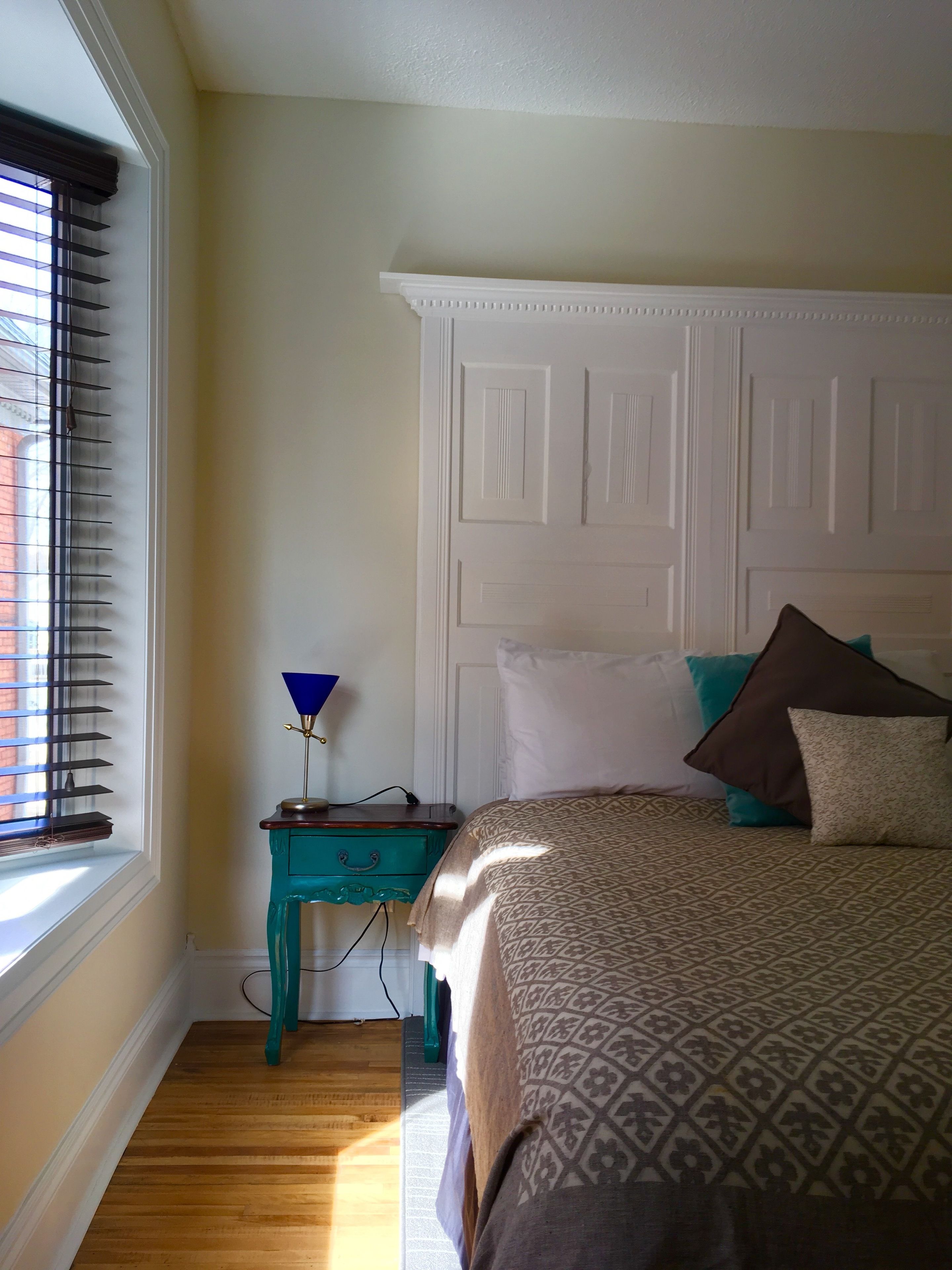 A bedroom with a bed, a nightstand, a lamp, and a window with blinds.