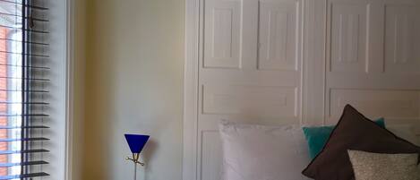 A bedroom with a bed, a nightstand, a lamp, and a window with blinds.