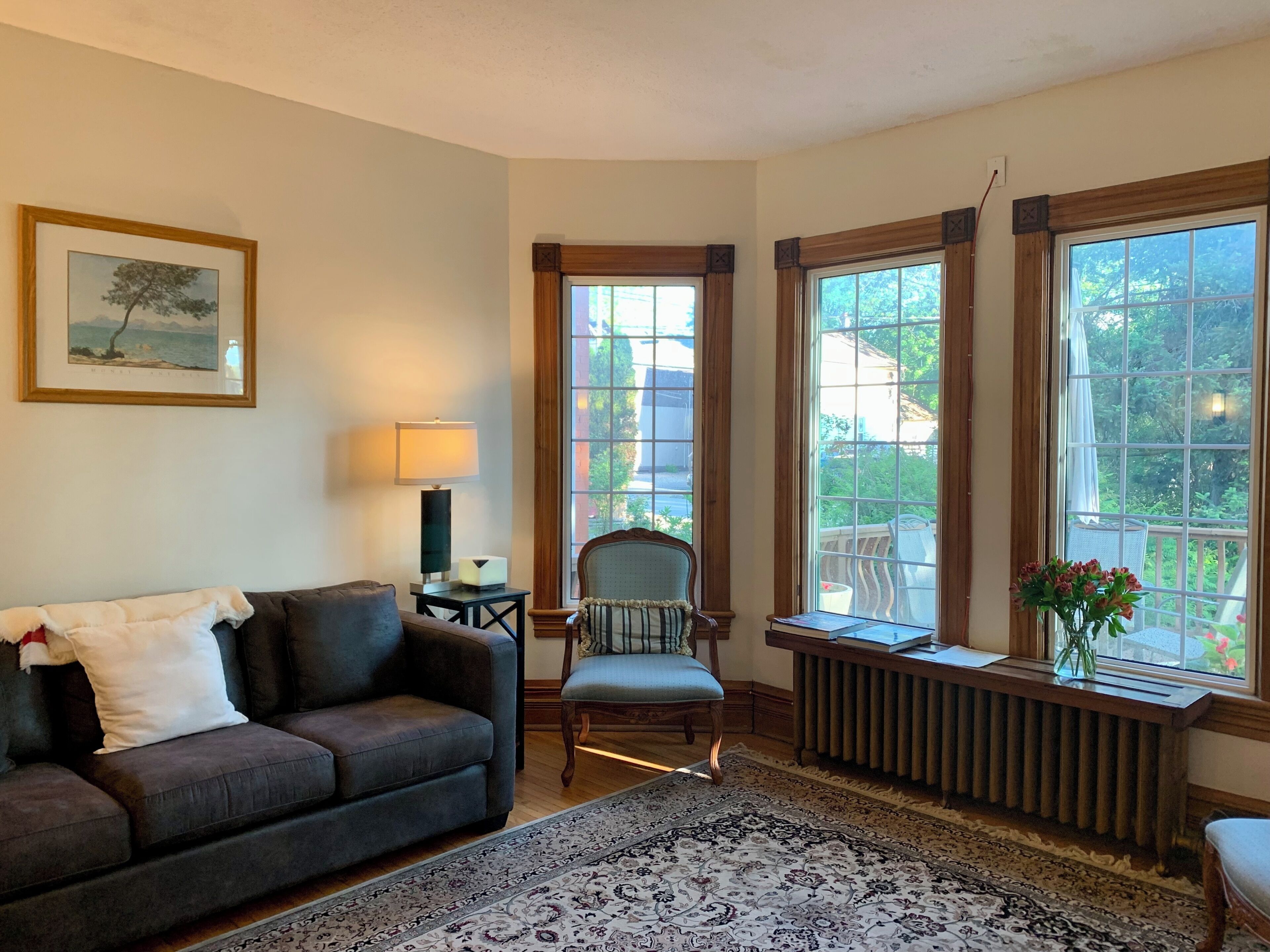 A living room with a sofa, armchair, table, lamp, and a large window with a view of greenery.