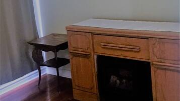 A room with a wooden desk, a small table, a patterned rug, and a framed picture on the wall.