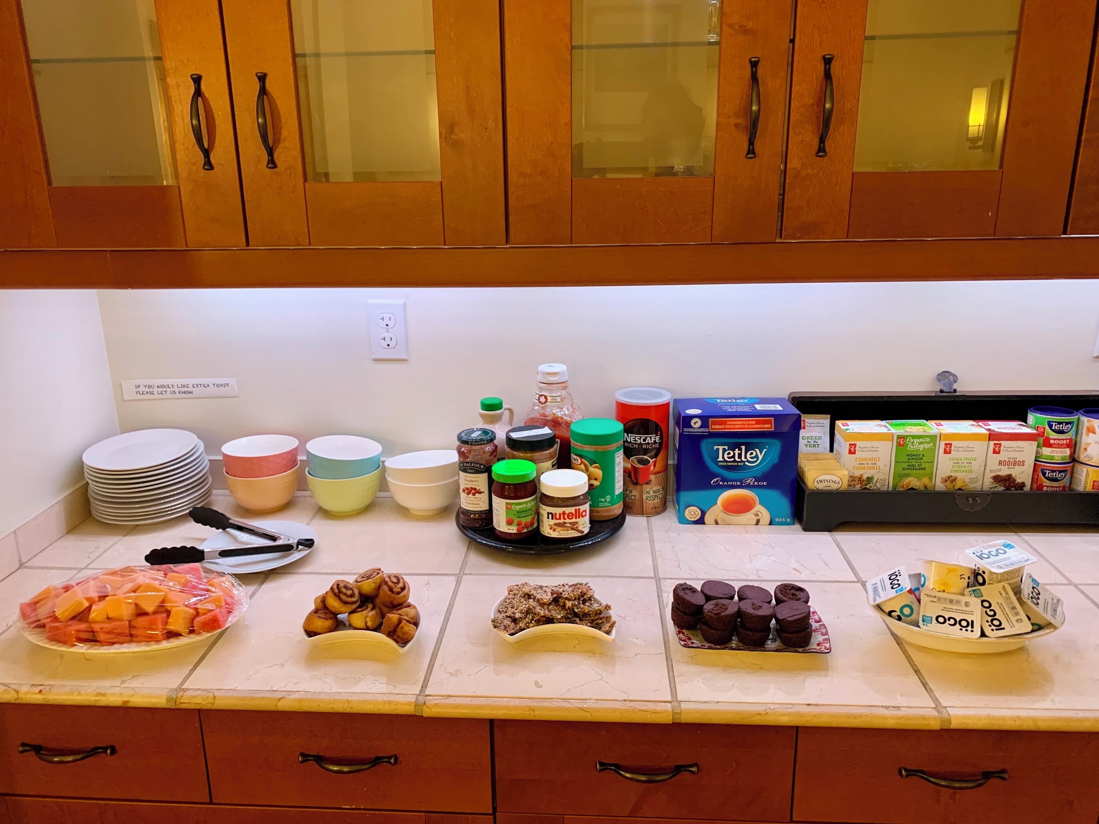 A kitchen counter with various food items, including jars of spreads, a bowl of fruit, and boxes of cereal.