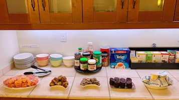 A kitchen counter with various food items, including jars of spreads, a bowl of fruit, and boxes of cereal.
