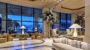 A spacious lobby with large windows, a palm tree, and a beige sofa. - Hotel Las Arenas Balneario Resort (Valencia)