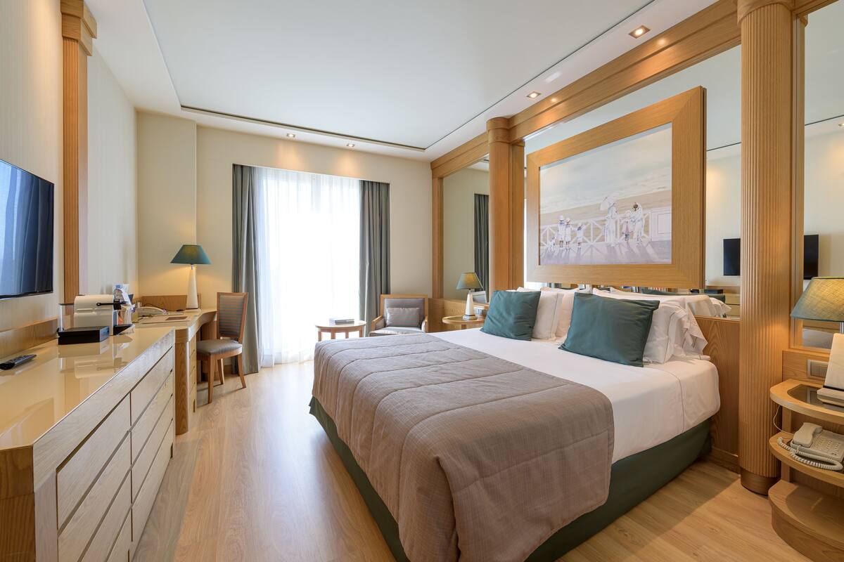 Hotelkamer met een groot bed, een bureau met een computer, een stoel, een televisie en een schilderij aan de muur.