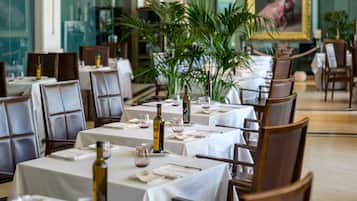 Un restaurant où les tables sont dressées pour le service, avec une composition florale au centre et un tableau accroché au mur.