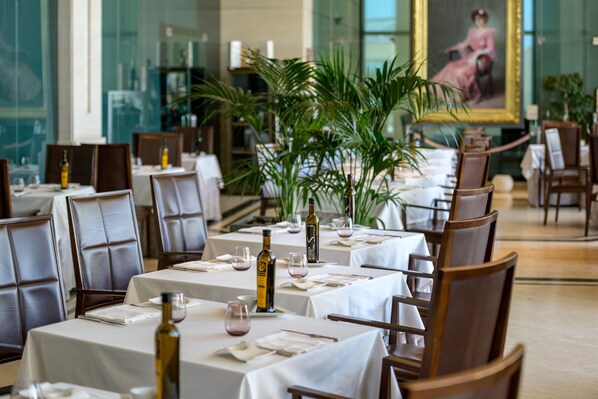A restaurant with tables set for dining, featuring a central plant arrangement and a painting on the wall.