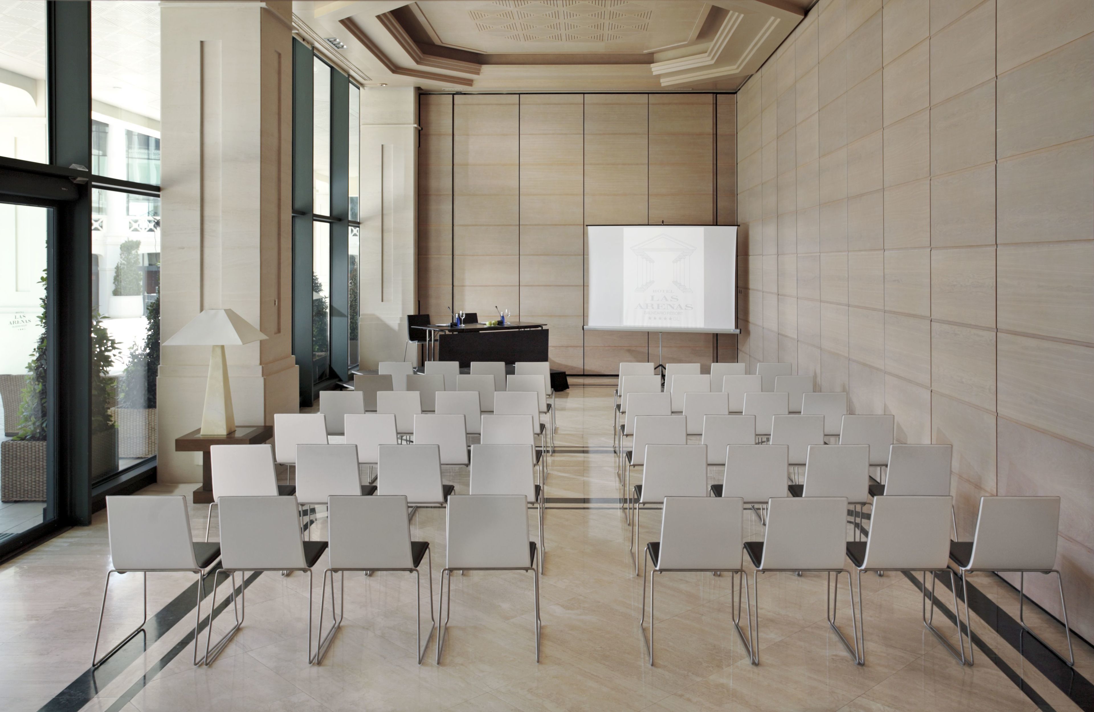 Une salle de conférence avec des rangées de chaises blanches, un écran de projection et un pupitre pour les présentations.