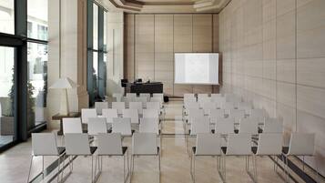Une salle de conférence avec des rangées de chaises blanches, un écran de projection et un pupitre pour les présentations.