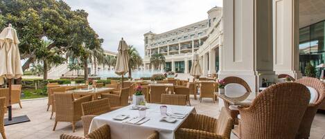 An outdoor dining area with wicker furniture and a view of a large building with multiple floors and balconies.