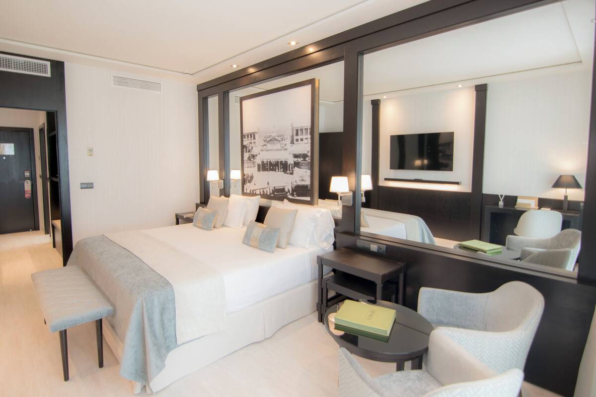 Een hotelkamer met een groot bed, nachtkastjes, een bureau, een stoel, een spiegel en een televisie.