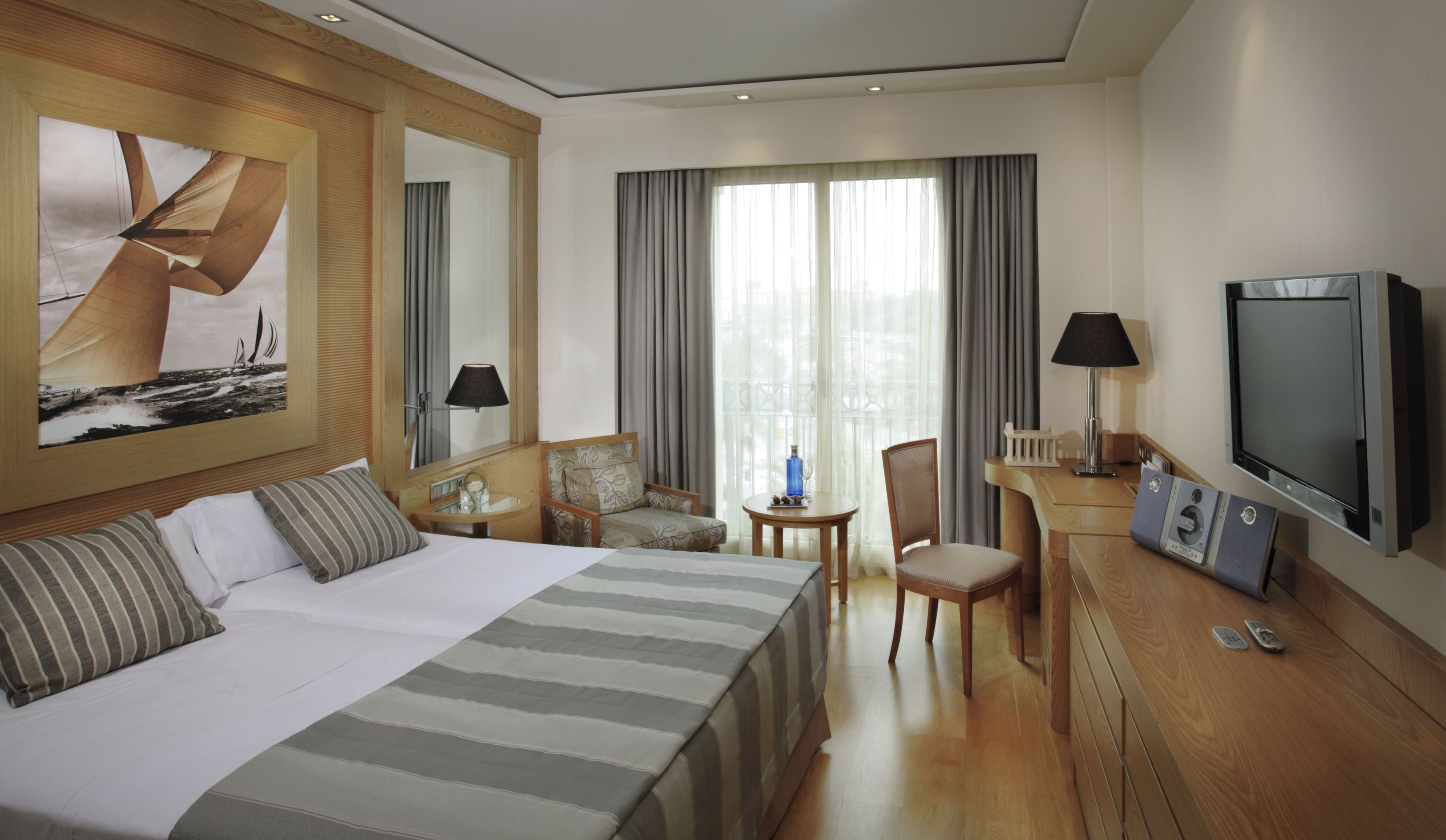 Habitación de hotel con una cama grande, un escritorio con televisor, una silla y una mesita de noche con lámpara.