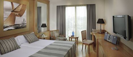 Habitación de hotel con una cama grande, un escritorio con televisor, una silla y una mesita de noche con lámpara.