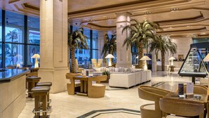 A spacious lobby with a bar area, seating arrangements, and large windows offering views of palm trees. - Hotel Las Arenas Balneario Resort (Valencia)