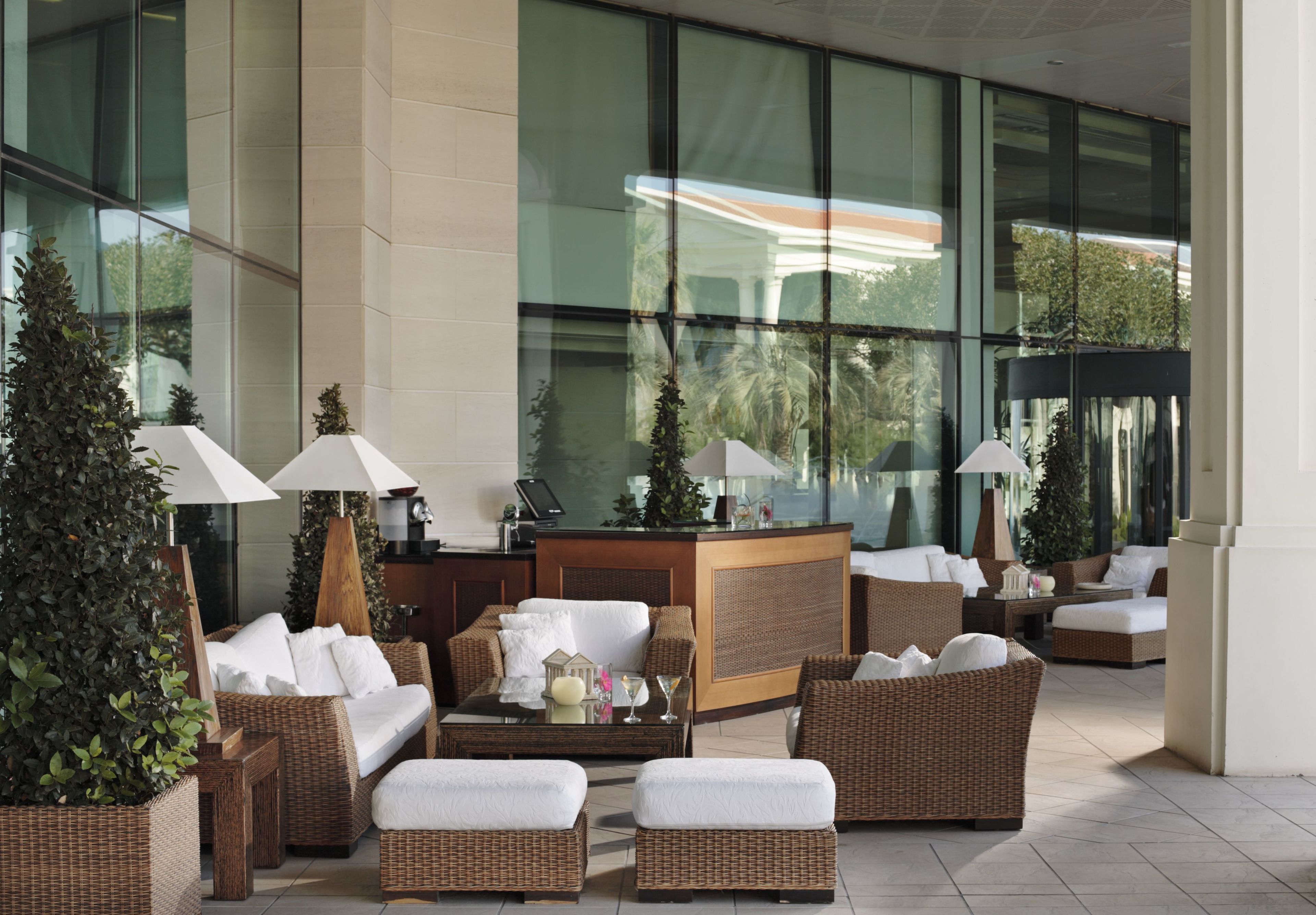 A modern lobby with wicker furniture, a reception desk, and large windows offering views of greenery.