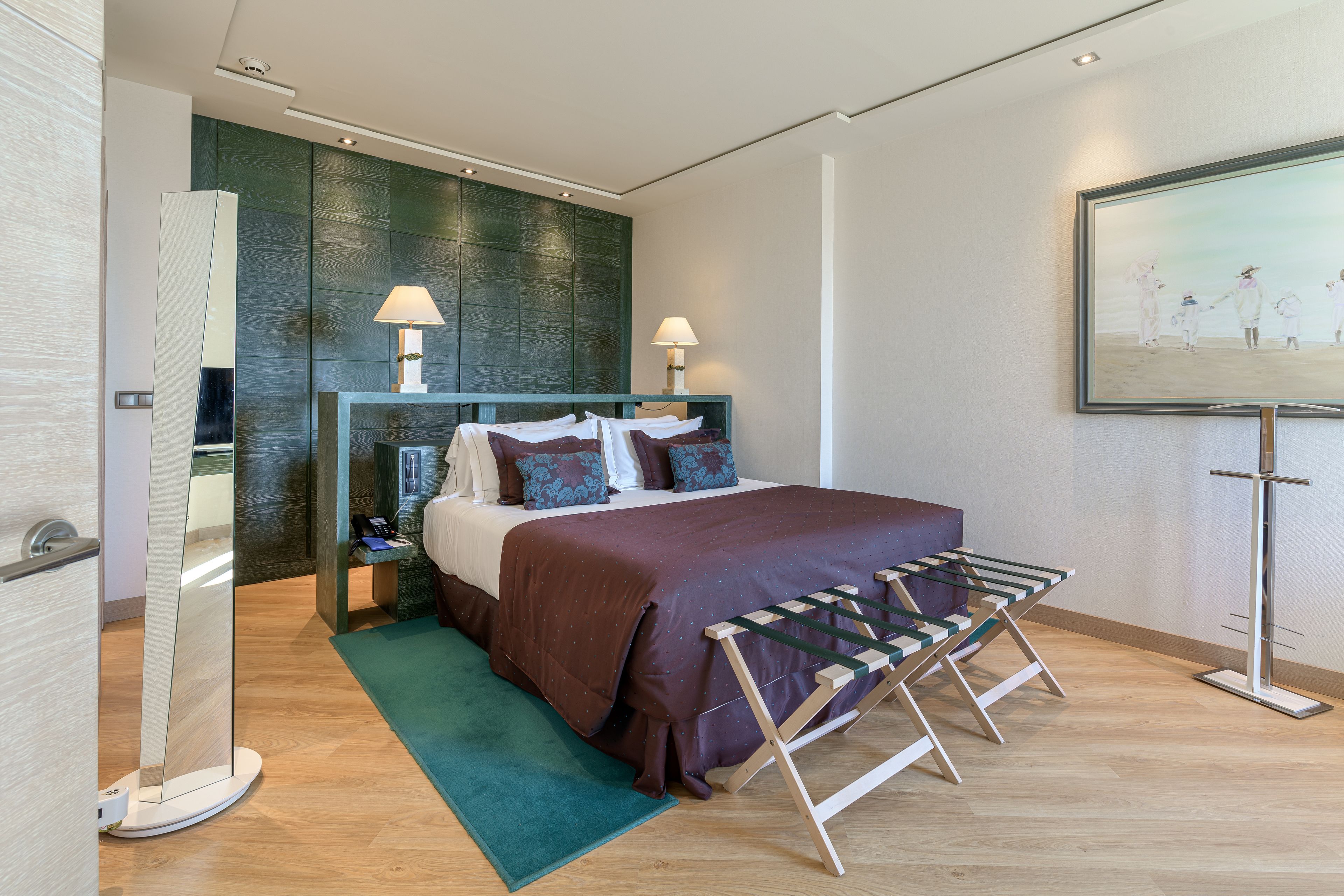 Habitación de hotel moderna con una cama grande, dos lámparas de noche, un panel de pared verde, un cuadro y un tendedero de madera.