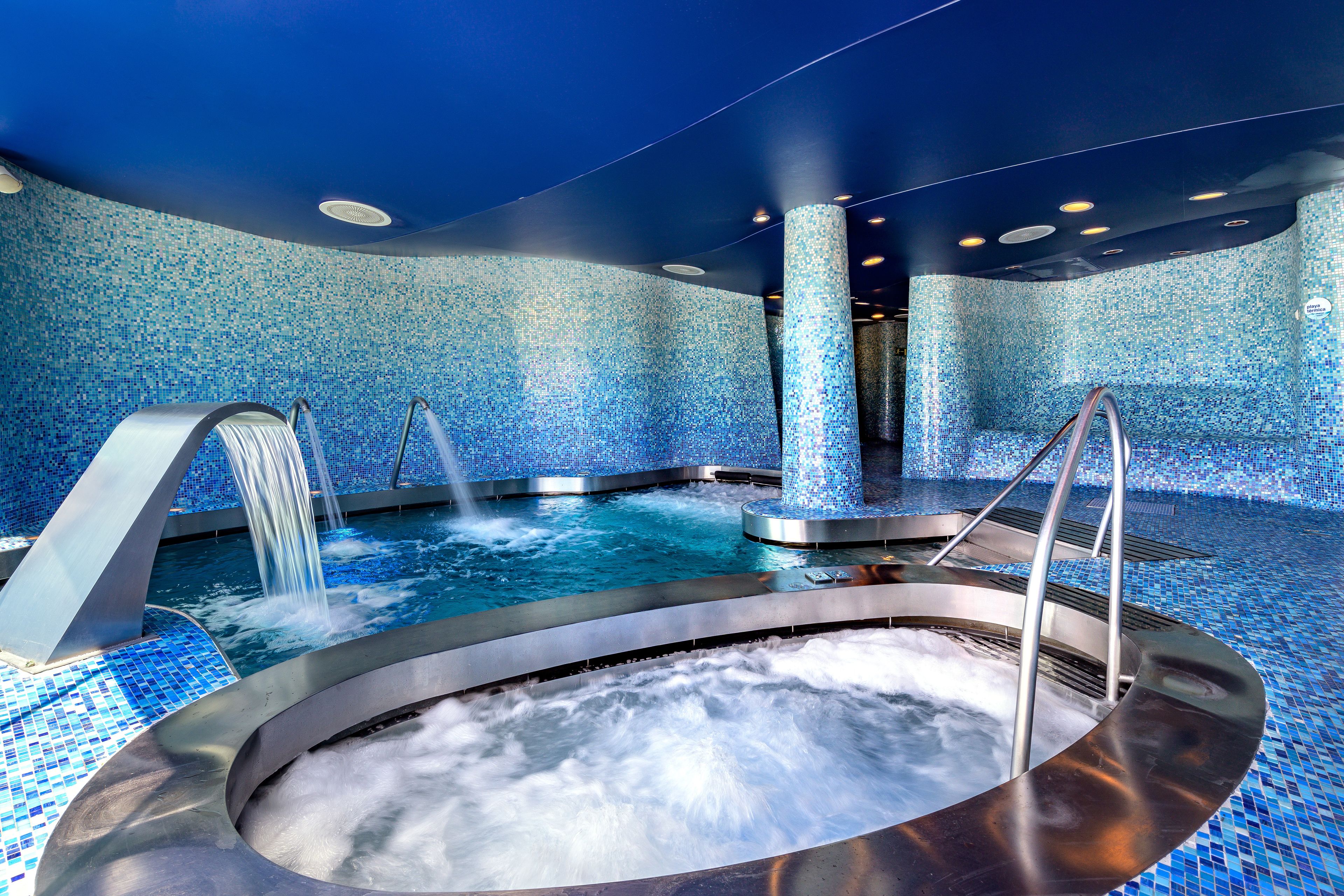 Un área de spa con un jacuzzi, una pequeña cascada y una pared de azulejos.