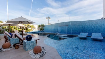 Zona de piscina con sillones de descanso, sombrillas y una fuente de agua.
