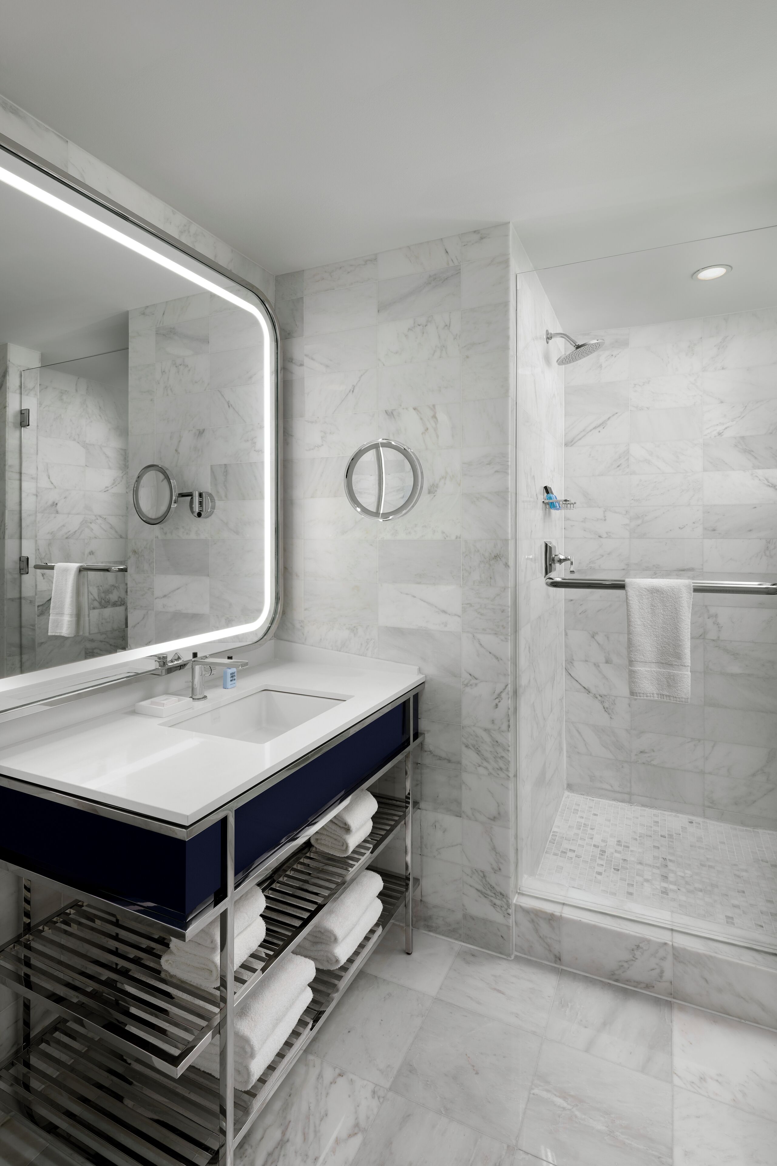 Une salle de bain moderne avec un grand miroir, un lavabo, une douche et un porte-serviettes.