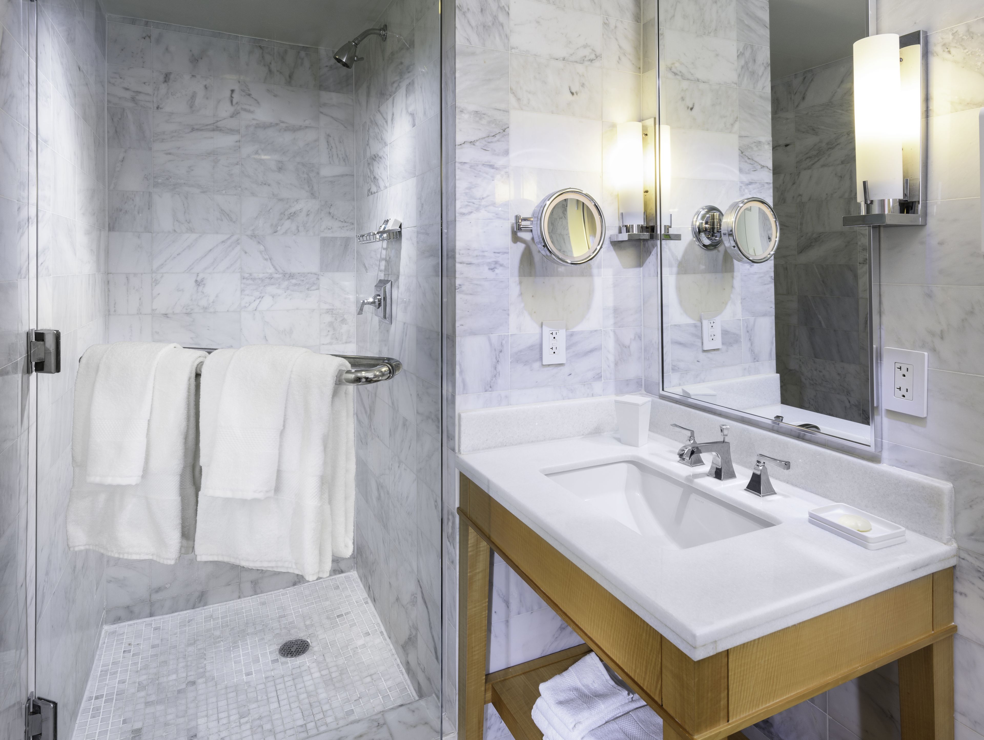 A modern bathroom with a glass shower enclosure, a wooden vanity with two sinks, and a large mirror.