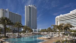 Un hotel con un amplio espacio de piscina, palmeras y edificios modernos al fondo.