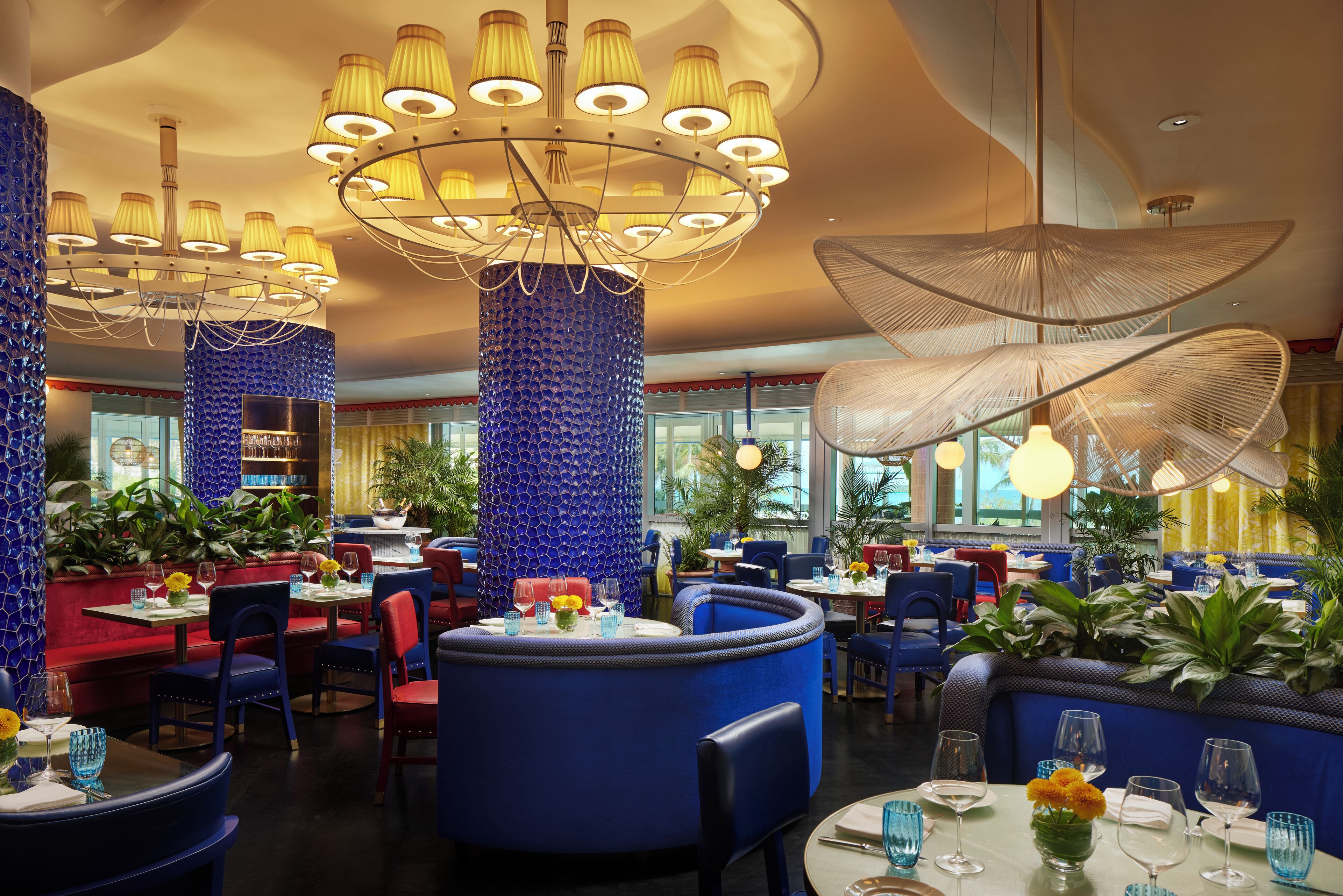 A restaurant interior with round tables, blue and red seating, and decorative lighting fixtures.