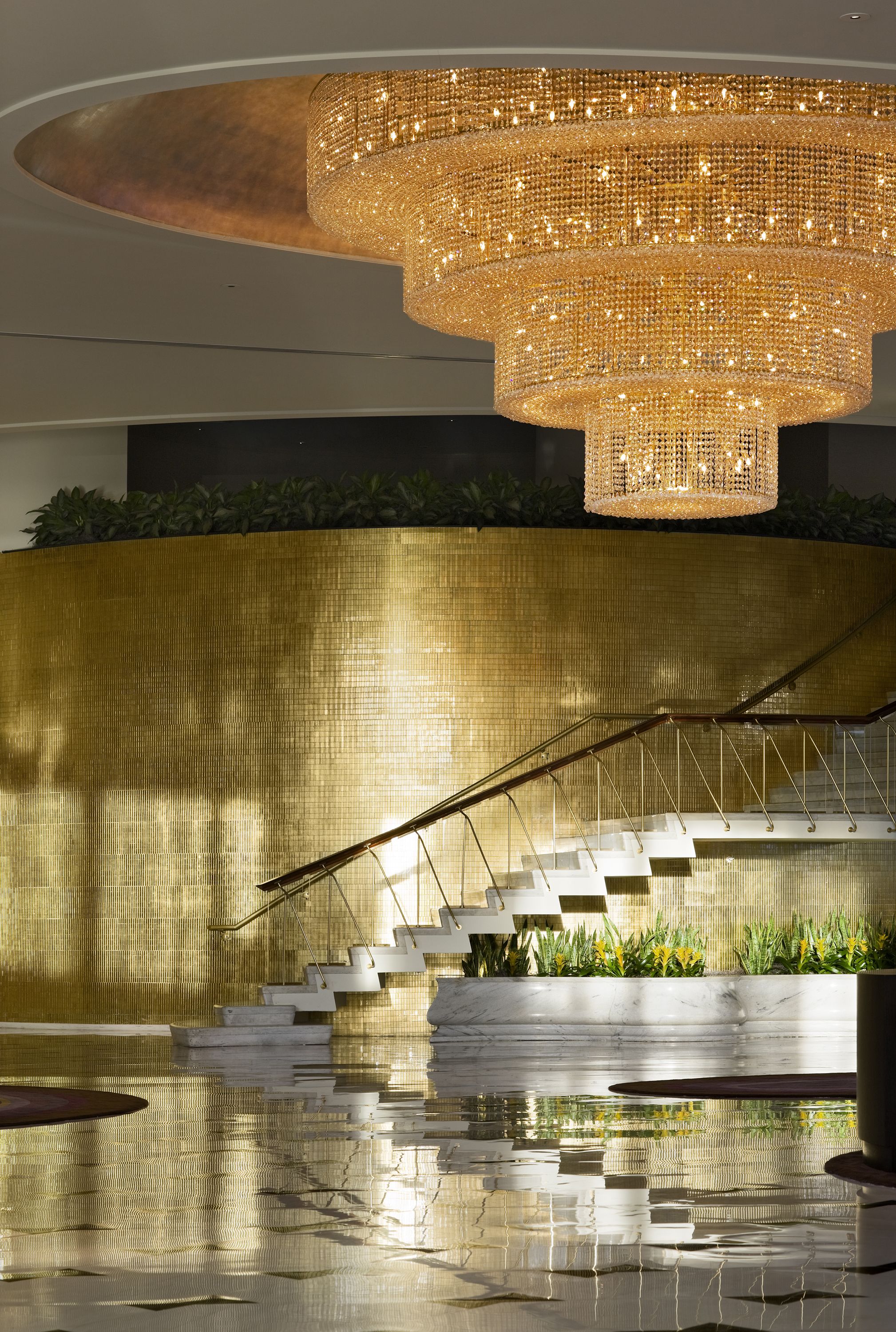 Ein prächtiger Kronleuchter, eine Marmortreppe und eine spiegelnde Wasserspielelement in einer modernen Lobby.