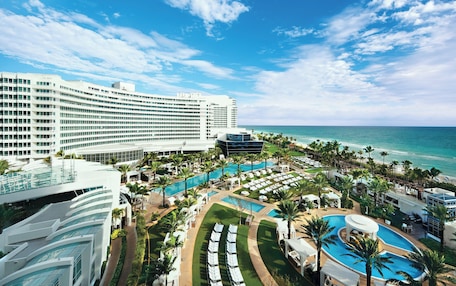 A resort with multiple swimming pools, a large hotel building, and a beach view.