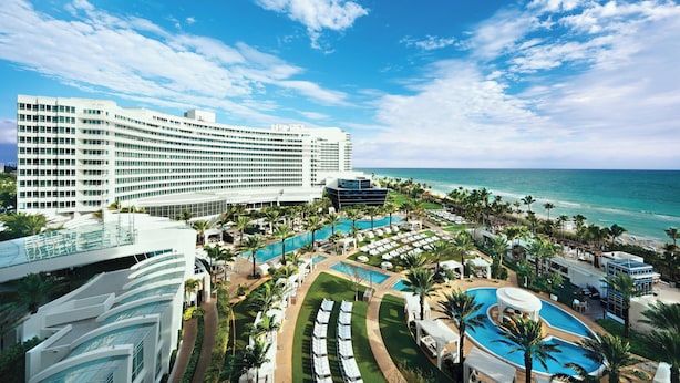 Un resort con varias piscinas, un gran edificio de hotel y vista a la playa.